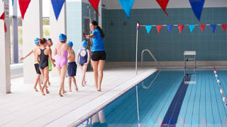 Vrouwelijke zwemcoach begeleidt kinderen naast het zwembad